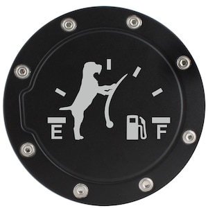 May include: A circular black fuel door cover featuring a silver graphic of a dog standing on its hind legs, mimicking a fuel gauge needle pointing toward the F. The design includes the letters E and F and a fuel pump icon, secured by eight bolts.