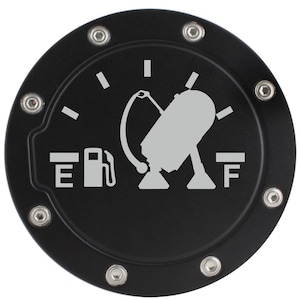 May include: Black circular fuel door cover with a silver graphic of a fuel gauge and a gas pump. The cover has a series of silver rivets around the edge. The gauge shows the fuel tank is nearly full.