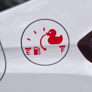 May include: A red vinyl decal applied to a white car fuel door, featuring a fuel gauge design. The graphic includes the letters E and F, a gas pump icon, and a rubber duck silhouette connected to the gauge needle by a curved line.