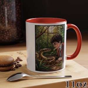 May include: White ceramic mug with a red interior and handle. The mug features a colorful illustration of a boy with glasses and a snake. The mug is labeled "11oz".