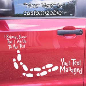 May include: A white vinyl decal applied to a red car door. The decal features white footprints and text that reads: I SOLEMNLY SWEAR THAT I AM UP TO YOUR TEXT and Your Text Managed. The text "Your Text" is customizable for the user's preference.