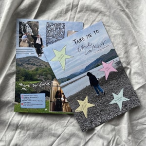 K&ouml;nnte beinhalten: Eine Zine mit dem Titel "Take Me To The Lakes" mit einem rosa, gr&uuml;nen und gelben Stern-Aufkleber auf dem Cover. Die Zine ist ge&ouml;ffnet und zeigt eine Seite mit einem Foto eines Sees und einer Person, die am Ufer entlangl&auml;uft. Die Seite enth&auml;lt auch eine Liste von Orten, an denen man die Zine finden kann.