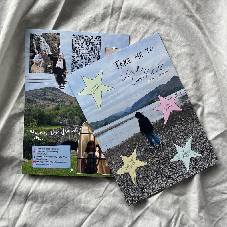 K&ouml;nnte beinhalten: Eine Zine mit dem Titel "Take Me To The Lakes" mit einem rosa, gr&uuml;nen und gelben Stern-Aufkleber auf dem Cover. Die Zine ist ge&ouml;ffnet und zeigt eine Seite mit einem Foto eines Sees und einer Person, die am Ufer entlangl&auml;uft. Die Seite enth&auml;lt auch eine Liste von Orten, an denen man die Zine finden kann.