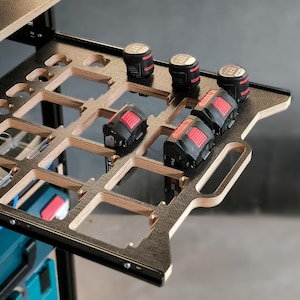 Könnte beinhalten: Ein Batterie-Aufbewahrungssystem aus Holz mit mehreren Steckplätzen zum Aufbewahren von Batterien. Das Gestell ist schwarz mit Holzverkleidung und hat einen Griff. In den Steckplätzen befinden sich mehrere schwarze und rote Batterien.