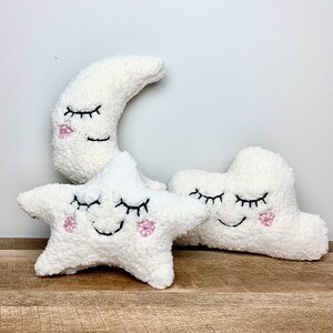 Op de afbeelding: Drie pluche speelgoedjes in de vorm van een halve maan, een ster en een wolk. Elk speelgoed heeft geborduurde ogen en een glimlachende mond met roze wangen.