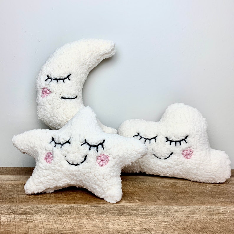 Op de afbeelding: Drie pluche speelgoedjes in de vorm van een halve maan, een ster en een wolk. Elk speelgoed heeft geborduurde ogen en een glimlachende mond met roze wangen.