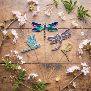 May include: Four stained glass dragonfly ornaments on thin metal stakes. One features iridescent blue and green wings, one has light blue textured wings, one is purple with striped wings, and one is yellow with a delicate wing pattern.