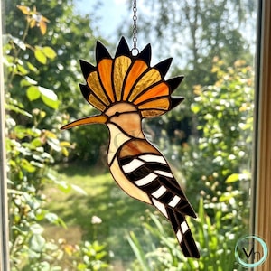 Può includere: Suncatcher a forma di uccello upupa in vetro colorato. L'uccello ha un becco lungo e curvo e una cresta a forma di ventaglio con dettagli arancioni e neri. Il corpo è un mix di beige, bianco e nero, con una catena per appenderlo. Decorazione per finestre.