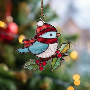 Può includere: Un ornamento natalizio a forma di uccello in vetro colorato. L'uccello indossa un cappello e una sciarpa rossi e bianchi, con un corpo blu e bianco. È posato su un ramo di agrifoglio con bacche rosse. L'ornamento è appeso a una catena d'oro.
