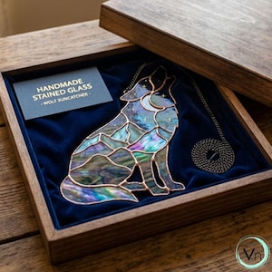 May include: A handmade stained glass wolf suncatcher in a wooden box. The wolf is howling at the moon and stars, with iridescent glass in shades of blue, green, and purple. The suncatcher is displayed on a blue velvet surface.