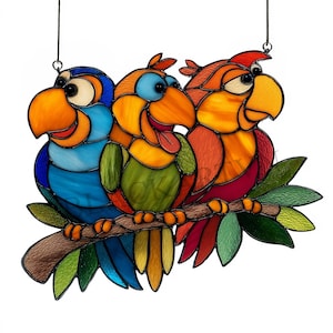 May include: Stained glass artwork featuring three colorful parrots perched on a branch. The parrots have vibrant blue, orange, green, and red plumage. The artwork is designed to hang, with a dark wire for display.