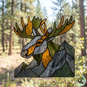 May include: A stained glass suncatcher depicting a moose head with large antlers in shades of amber and green, positioned above a mountain range crafted from dark green and grey glass pieces, all held together by dark metal solder lines.