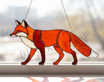Peut inclure: Suncatcher en vitrail représentant un renard aux tons orange, rouge et blanc, avec une chaîne pour l'accrocher. Le renard est représenté en position de marche, avec un travail du verre détaillé créant un aspect texturé. Une pièce décorative pour fenêtres ou murs.