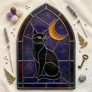 May include: A stained glass panel in a pointed arch shape featuring a black cat silhouette against a deep purple night sky with a yellow crescent moon and etched star details. The piece is framed in dark metal lead lines with a smooth finish.