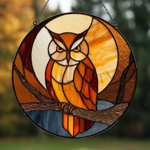 May include: A round stained glass window featuring an owl perched on a branch. The owl is depicted in shades of orange, brown, and yellow, with a backdrop of a moon and trees. The window is suspended by a chain.