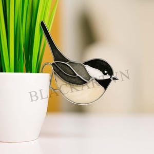 May include: A decorative bird ornament with a black, white, and gray design. The bird is perched on a white pot with green plants. The word "BLACKART" is partially visible on the pot.