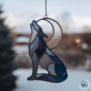 Könnte beinhalten: Glasmalerei eines heulenden Wolfs vor einem Mond. Der Wolf ist in Blautönen gehalten und sitzt vor einem Halbmond. Das Kunstwerk ist an einer Kette aufgehängt und eignet sich zur Dekoration von Fenstern oder Wänden.