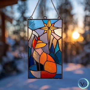 Puede incluir: Panel de vidrieras con un zorro, una estrella y una escena de montaña. La obra de arte utiliza colores naranja, azul, amarillo y morado. El panel es rectangular y cuelga de una cadena. El fondo está borroso, lo que sugiere un entorno al aire libre.
