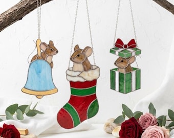Op de afbeelding: Drie glas-in-lood ornamenten hangend aan een tak. Eén toont een muis met een blauwe bel, een andere een muis in een rood-groene kerstsok, en de derde een muis in een groen cadeau met een rode strik. Elk ornament heeft een zilveren ketting.