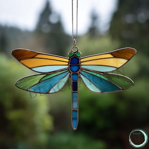 Pode incluir: Um apanhador de sol de vitral em forma de libélula, com uma moldura cor de cobre. As asas apresentam tons de amarelo, azul e verde. A libélula é suspensa por uma corrente delicada, ideal para uma janela ou parede.