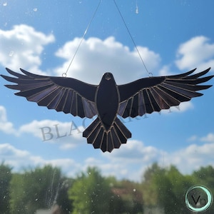 May include: A stained glass raven with outstretched wings, suspended by wires against a blue sky with clouds. The raven is primarily black with hints of purple and grey. The word "BLAC" is partially visible.