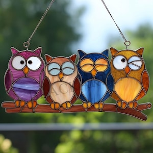 Peut inclure: Panneau en vitrail représentant quatre hiboux colorés perchés sur une branche marron. Les hiboux sont de différentes couleurs, notamment violet, marron, bleu et or, avec des yeux blancs et noirs. Le panneau est conçu pour être suspendu et convient à la décoration intérieure.