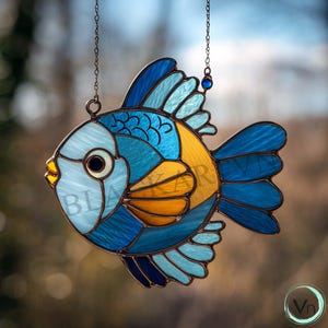 May include: A stained glass fish suncatcher in shades of blue, yellow, and teal, with a copper-colored frame and hanging chain. The fish has a round eye and a detailed fin design. The word "BLANKAR" is visible on the fish.