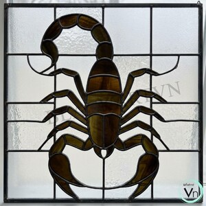 May include: Stained glass panel featuring a scorpion design. The scorpion is depicted in shades of brown and amber, with a detailed segmented body and curved tail. The panel is framed by a black grid, creating a window-like appearance. The background is a frosted glass.