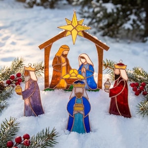 May include: A stained glass nativity scene featuring a central stable structure with a yellow star, figures of two adults and a child in a manger, and three standing figures in purple, blue, and red robes, all with metallic outlines.