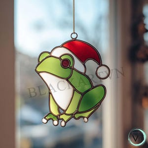Puede incluir: Adorno de rana de vidriera con gorro de Papá Noel. La rana es verde, blanca y marrón con un gorro rojo y blanco. El adorno cuelga de un cordón dorado. Diseñado para colgar en una ventana.
