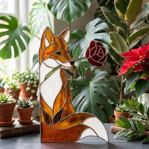 May include: Stained glass fox figurine in shades of orange, brown, and white, holding a red rose. The fox is a decorative item, perfect for home decor. The figurine is approximately 25 cm tall.