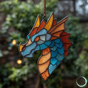Op de afbeelding: Een gebrandschilderd glazen drakenkopornament met een bruin ophangkoord. De draak heeft een mozaïekontwerp in tinten blauw, oranje en geel, met een donker metalen frame. Het ornament is ontworpen om op te hangen.
