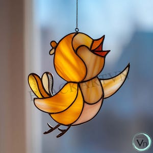 Op de afbeelding: Een gebrandschilderde vogel zonnevanger met een vrolijk ontwerp. De vogel heeft tinten geel, oranje en een vleugje rood. De vleugels zijn uitgespreid en de vogel hangt aan een dunne zwarte ketting. Het ontwerp is speels en decoratief.