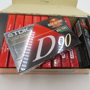 May include: A box of 10 TDK D90 audio cassette tapes. The tapes are red and black with the text "TDK D90" printed on them. The box is open and the tapes are visible inside.
