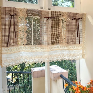 Puede incluir: Una cenefa de ventana con un diseño de patchwork. Presenta paneles de tela a cuadros, encaje y telas lisas en tonos marrones, beige y blanco. Los lazos decorativos y los bordes de encaje añaden detalles.
