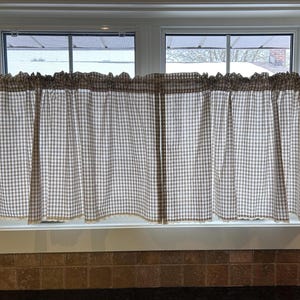 K&ouml;nnte beinhalten: Fenstervorh&auml;nge mit einem braun-wei&szlig; karierten Muster. Die Vorh&auml;nge h&auml;ngen an einer Stange &uuml;ber einem Fenster. Der untere Rand der Vorh&auml;nge hat eine dekorative Bord&uuml;re.