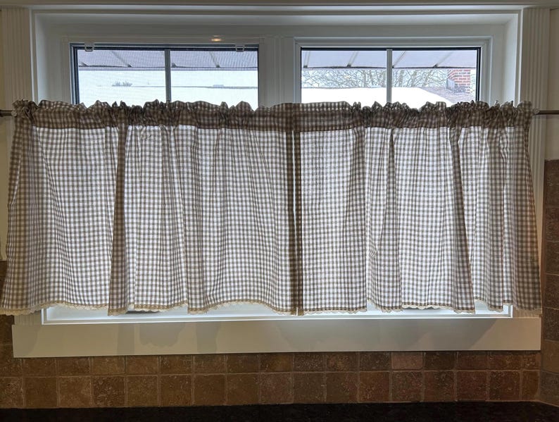 K&ouml;nnte beinhalten: Fenstervorh&auml;nge mit einem braun-wei&szlig; karierten Muster. Die Vorh&auml;nge h&auml;ngen an einer Stange &uuml;ber einem Fenster. Der untere Rand der Vorh&auml;nge hat eine dekorative Bord&uuml;re.