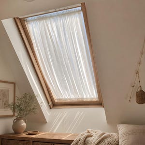 Pode incluir: Uma cortina de tecido branco semitransparente instalada numa janela de telhado inclinada com moldura de madeira. A cortina apresenta um design franzido e plissado que pende verticalmente, permitindo que a luz natural se filtre suavemente.