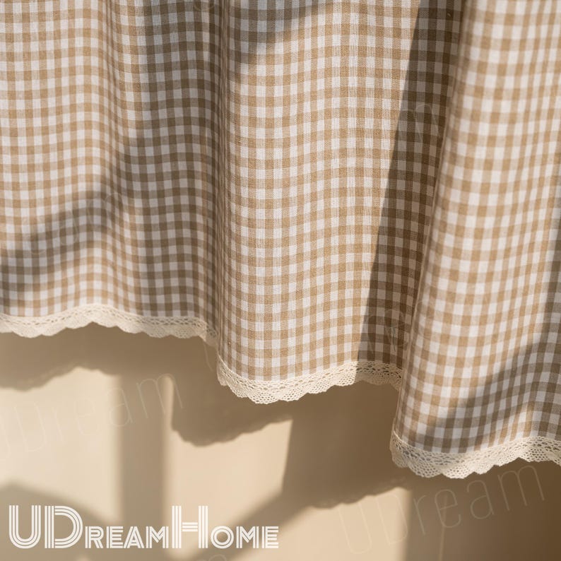 K&ouml;nnte beinhalten: Beige-wei&szlig; karierter Vorhang mit zarter Spitzenborte am unteren Rand. Der Stoff ist drapiert und erzeugt weiche Falten und Schatten. Der Vorhang ist wahrscheinlich f&uuml;r ein Fenster oder einen T&uuml;rrahmen.