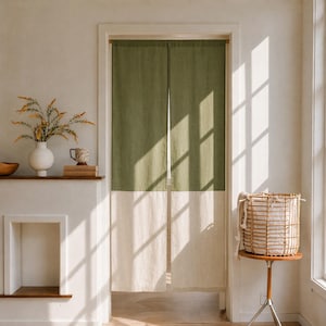 May include: A two-toned door curtain featuring a solid olive green upper section and a solid off-white lower section. The rectangular fabric panel hangs vertically within a doorway, split down the center to create two distinct fabric panels.