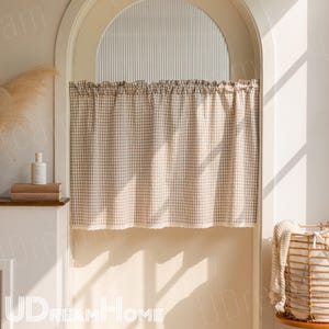 K&ouml;nnte beinhalten: Ein beige-wei&szlig; karierter K&uuml;chenvorhang mit ger&uuml;schtem Oberteil und Spitzenbesatz am unteren Rand. Der Vorhang h&auml;ngt in einem bogenf&ouml;rmigen T&uuml;rrahmen, mit Sonnenlicht von rechts. Die Worte "UDREAMHome" sind unten sichtbar. Der Vorhang ist ca. 100 cm breit.
