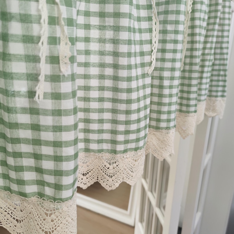 May include: Green and white gingham check curtains with cream lace trim. The curtains are hanging, showing a close-up of the fabric's texture. The design is a classic, country-style pattern, with a delicate lace border.