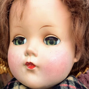 May include: A vintage porcelain doll with brown hair, wearing a plaid shirt and a straw hat. The doll has blue eyes and rosy cheeks.