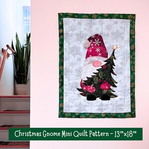 May include: A Christmas gnome mini quilt pattern with a green border and a white background featuring a gnome holding a Christmas tree. The text "Christmas Gnome Mini Quilt Pattern - 13"x18" is at the bottom of the image.