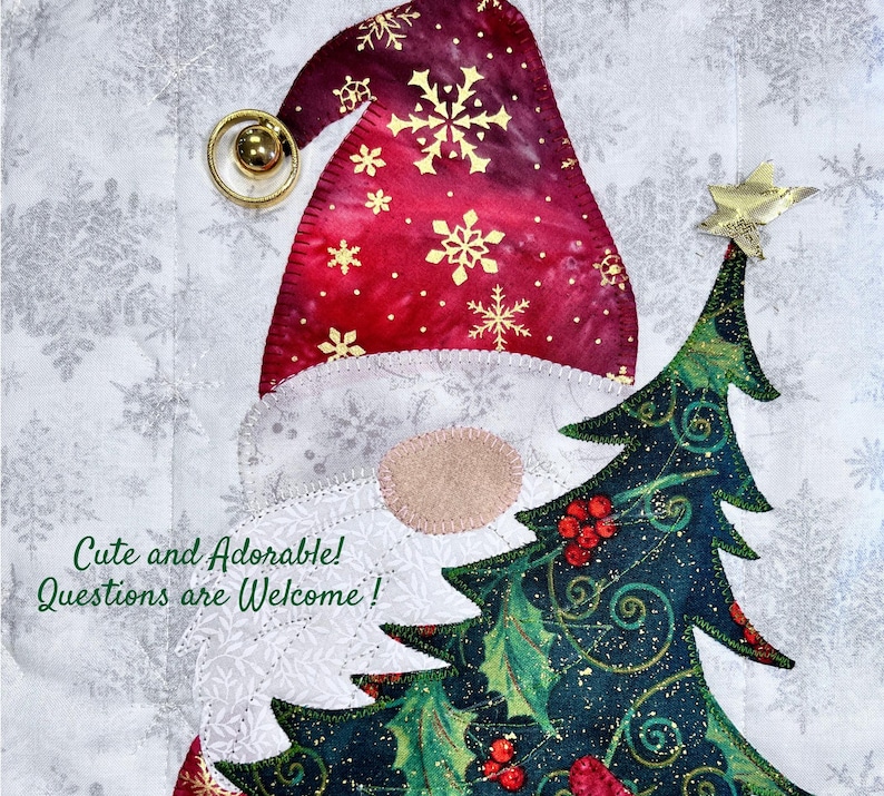May include: A festive Christmas quilt block featuring a Santa Claus with a red and gold hat and a green Christmas tree with red berries and gold glitter. The background is a white fabric with a snowflake pattern.