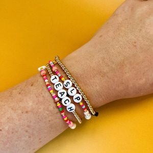 May include: A set of five bracelets with colorful beads and white letter beads spelling out "SLP TEACH".