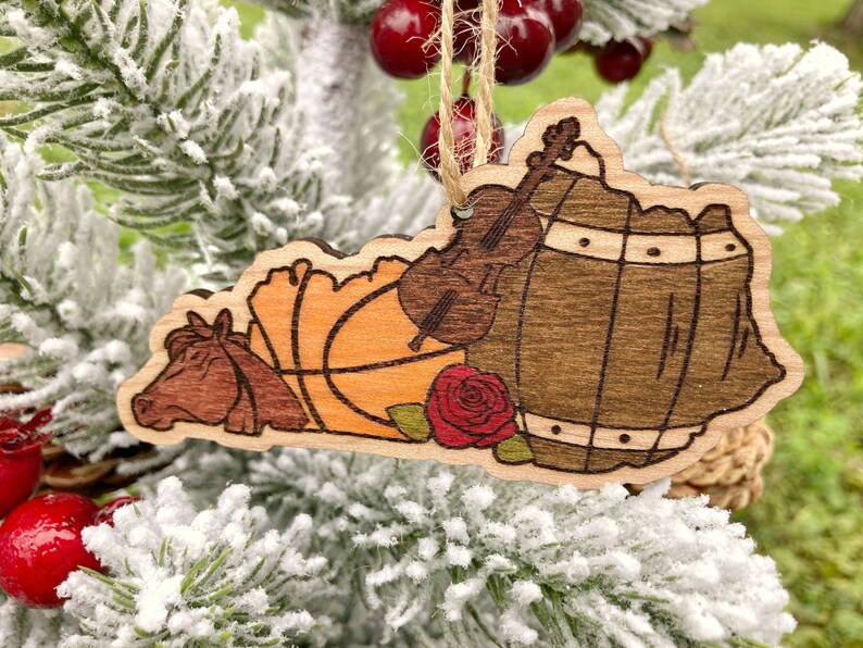 May include: Wooden ornament shaped like the state of Kentucky with a brown horse, an orange basketball, a brown barrel, a red rose, and a brown violin.