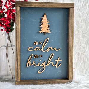May include: A wooden sign with a blue background and a wood cutout of a Christmas tree. The sign says "All is calm, All is bright".