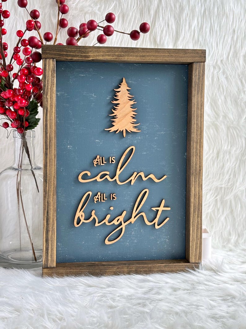 May include: A wooden sign with a blue background and a wood cutout of a Christmas tree. The sign says "All is calm, All is bright".