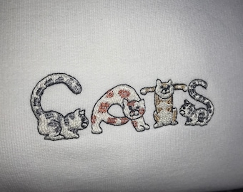 Puede incluir: Sudadera blanca con gatos bordados que deletrean la palabra "CATS".